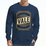 A man wearing a VALE Traveler’s Goods long-sleeve cotton shirt featuring a vintage-style gold and cream graphic label that says "Bound for Adventure" on the chest.