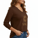 Front view of a woman wearing a VALE brand long sleeve V-neck cotton shirt featuring a gold celestial sun and moon logo, available in maroon, brown, and orange.