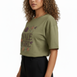 Young woman wearing a "Vale Girl" breathable cotton t-shirt with a vintage floral and hummingbird graphic design, available in Olive Green, Royal Blue, and Red.