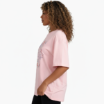 A young woman taking a mirror selfie wearing a VALE GIRL graphic t-shirt made of breathable cotton with a floral design, available in pink, light blue, and maroon.