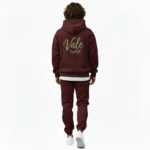 A man wearing a premium breathable cotton tracksuit featuring a sage green "Vale" script logo and olive branch graphic on the back, available in Black, Charcoal Grey, and Burgundy.