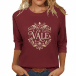 Woman wearing a breathable cotton 3/4 sleeve raglan shirt featuring a gold-toned floral "VALE" crest design, available in Navy Blue, Earthy Brown, and Maroon.