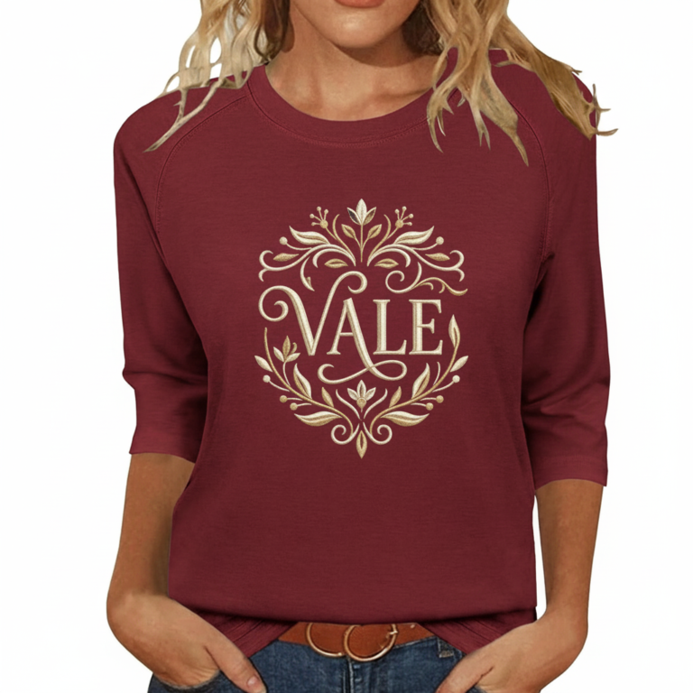 Woman wearing a breathable cotton 3/4 sleeve raglan shirt featuring a gold-toned floral "VALE" crest design, available in Navy Blue, Earthy Brown, and Maroon.