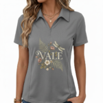 Female model wearing a slim-fit breathable cotton pique polo shirt featuring a "VALE" botanical graphic with ferns, flowers, and a dragonfly. Available in Forest Green, Charcoal Grey, and Earthy Brown.