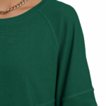 : A person wearing an oversized breathable cotton shirt featuring a "VALE" logo with colorful layered angel wings on the front, available in green, black, and purple.