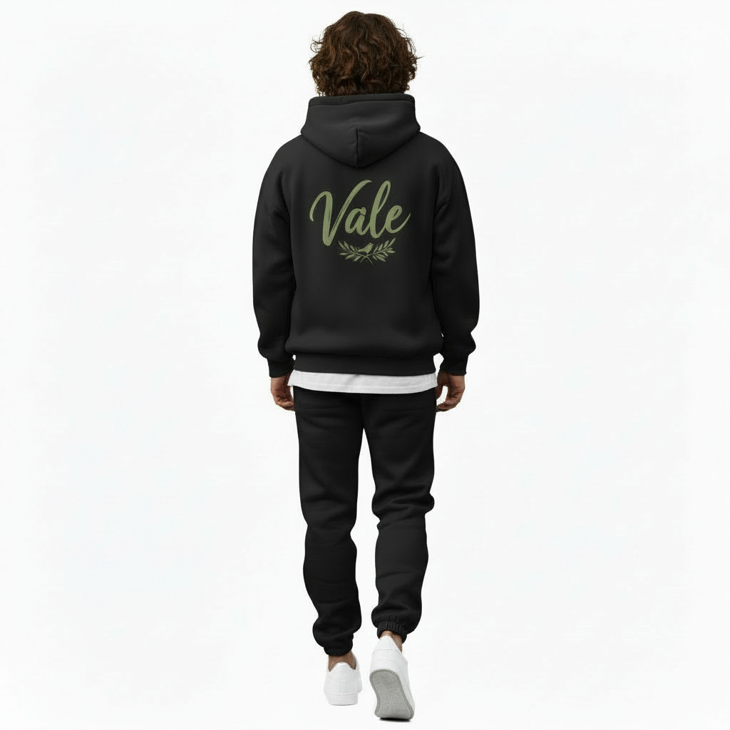 A man wearing a premium breathable cotton tracksuit featuring a sage green "Vale" script logo and olive branch graphic on the back, available in Black, Charcoal Grey, and Burgundy.