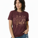 Woman wearing a Vale Authentic Style limited edition graphic t-shirt featuring rose gold butterfly and floral art on forest green, white, and burgundy cotton fabric.