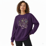 Woman wearing a VALE graphic cotton sweatshirt featuring a swallow, butterfly, and botanical nature design in Forest Green, Black, and Purple colors.