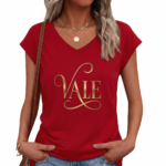 Professional studio shot of a woman wearing a VALE brand V-neck breathable cotton t-shirt with a metallic gold cursive logo, styled with denim jeans and gold accessories.