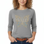 A woman wearing a VALE brand 3/4 sleeve raglan shirt made of breathable cotton, featuring a large, ornate butterfly embroidery on the chest in gold and light blue.