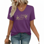 Close-up of a woman wearing a breathable cotton V-neck t-shirt featuring a gold floral "VALE" graphic and a small chest pocket, paired with blue jeans.