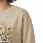Woman wearing a VALE graphic cotton sweatshirt with autumn leaf botanical design, available in Beige, Slate Blue, and Burnt Orange.