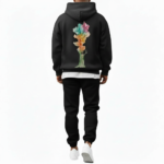 A man wearing a premium breathable cotton tracksuit featuring a colorful watercolor tree graphic with "VALE" text on the back, available in Black, Burgundy, and Sand.