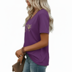 Close-up of a woman wearing a breathable cotton V-neck t-shirt featuring a gold floral "VALE" graphic and a small chest pocket, paired with blue jeans.