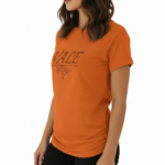 Woman wearing a VALE brand graphic t-shirt in breathable cotton, featuring a minimalist leaf design and athletic slim fit. Available in Black, Purple, and Orange.