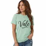Woman wearing a "Vale" script graphic t-shirt made of breathable cotton, paired with distressed denim jeans, available in Slate Blue, Heather Grey, and Mint Green.