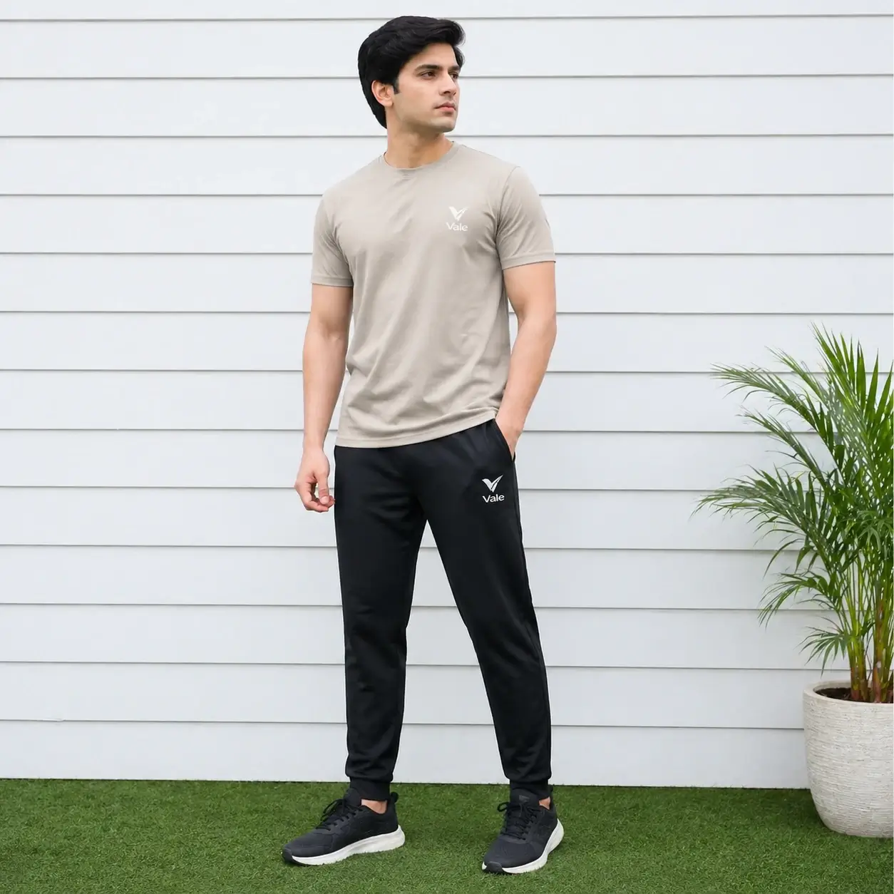 Vale men-beige-tshirt-black-track-pants-sportswear-model Men wearing beige t-shirt with black track pants sportswear outfit standing outdoors